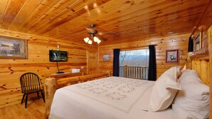 Une chambre à coucher dans une cabane en bois, avec un lit, une chaise, un bureau, un ventilateur de plafond et des tableaux encadrés accrochés aux murs.