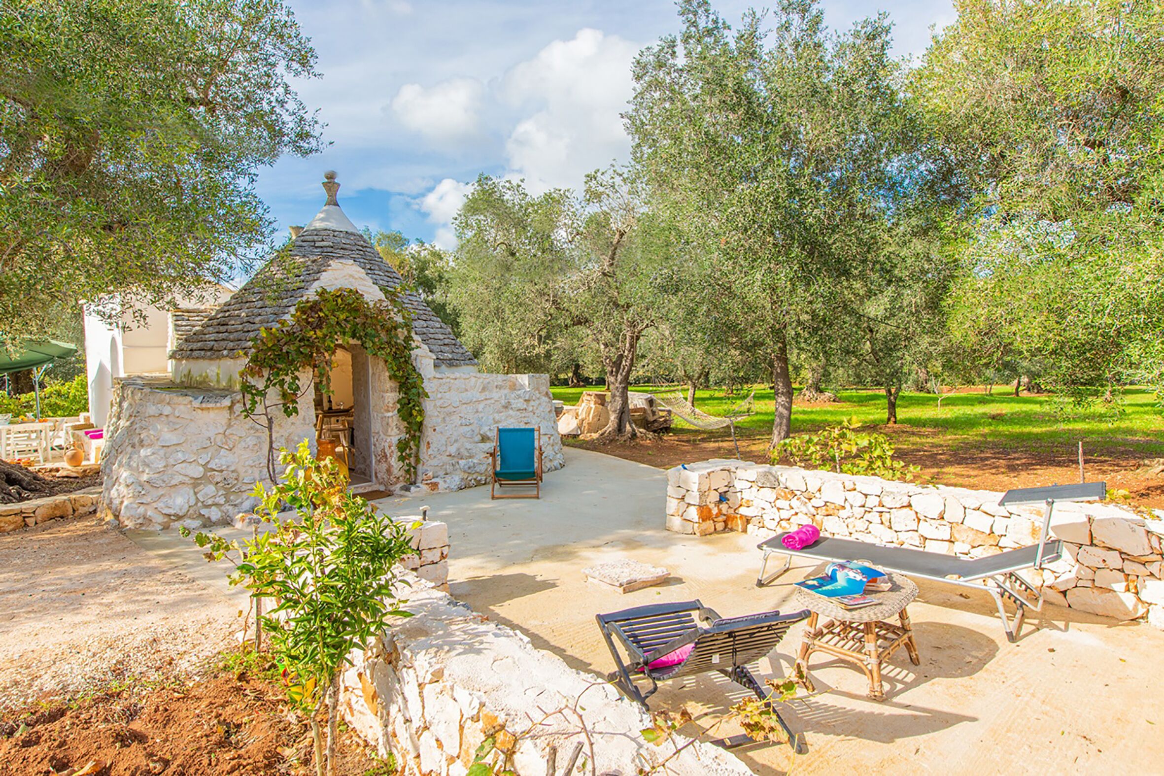 A stone-built outdoor area with a small structure, seating, and a stone wall.