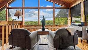 A cozy room with two grey armchairs, a small table with a lamp, and a large window offering a view of greenery. - Long range unobstructed views! Privacy, Hot tub, Close to town. Check reviews. (Sevierville)