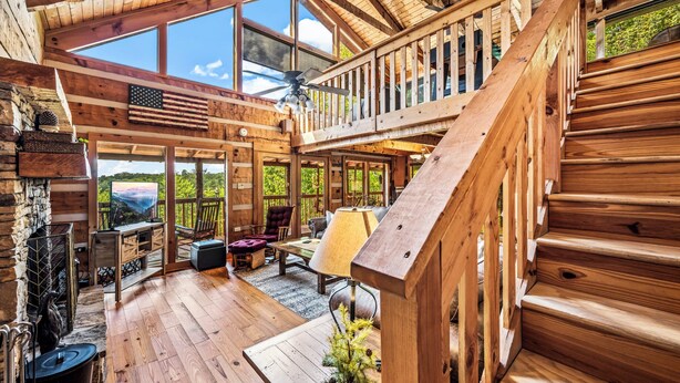 A wooden cabin with a fireplace, a dining area, and a staircase leading to a loft. - Long range unobstructed views! Privacy, Hot tub, Close to town. Check reviews. (Sevierville)