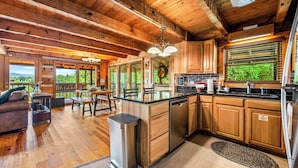 A spacious kitchen with wooden cabinets, a stainless steel dishwasher, and a large window overlooking greenery. - Long range unobstructed views! Privacy, Hot tub, Close to town. Check reviews. (Sevierville)