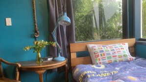 Un dormitorio con cama, un edredón con motivos espaciales, un escritorio de madera con lámpara, una silla y una ventana con cortinas.
