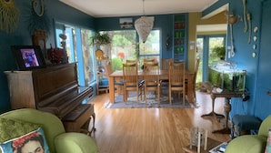 Una sala de estar acogedora con un piano de madera, sillones verdes, una mesa de comedor con sillas y un acuario.