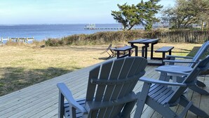 Une terrasse avec des fauteuils Adirondack et une table, donnant sur une pelouse et l’océan.