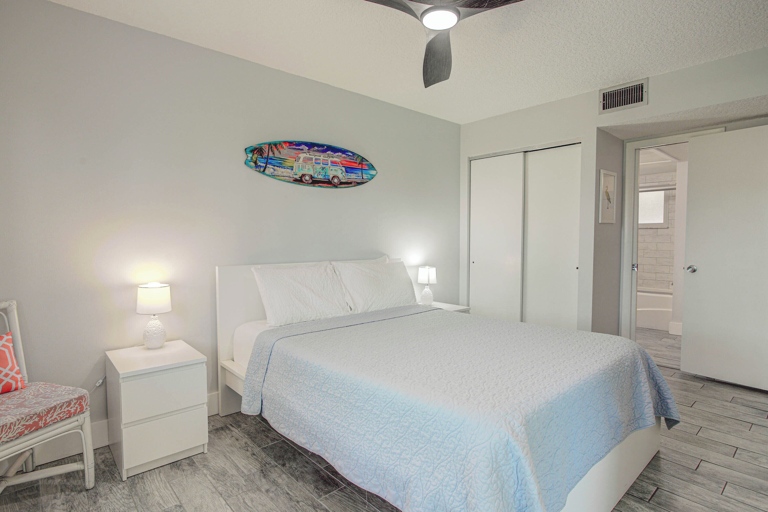 A bedroom with a bed, nightstands, a ceiling fan, a door, and a wall decoration.