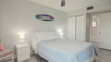 A bedroom with a bed, nightstands, a ceiling fan, a door, and a wall decoration.