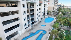 A multi-story building with a rooftop pool area, including two swimming pools and lounge chairs.