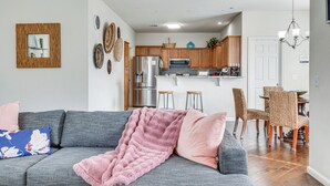Un soggiorno moderno con un divano grigio, una coperta rosa e un'area da pranzo con sedie in vimini e un tavolo in legno.