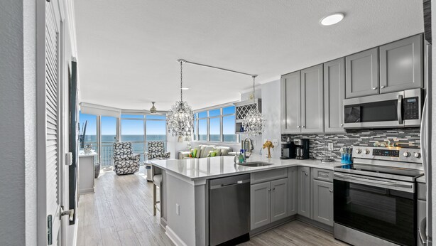 A modern kitchen with a large island, stainless steel appliances, and a view to the outside.
