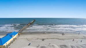 A beach with a pier extending into the ocean, a sandy beach, and a building with a blue roof.