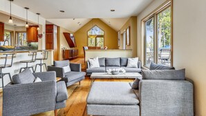 A spacious living area with a kitchen in the background, large windows, and a high ceiling.