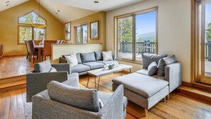 A spacious living room with a high ceiling, large windows, and a wooden floor.