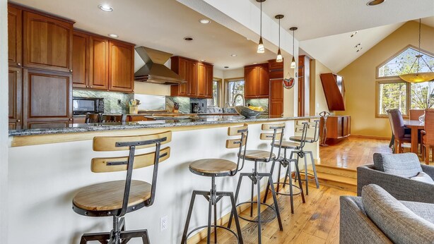A spacious kitchen with wooden cabinets, a central island with bar stools, and a dining area with a sofa and chairs.