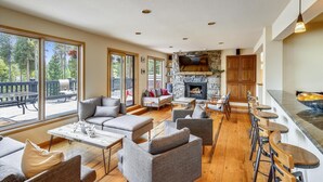 A spacious living room with a stone fireplace, comfortable seating, and large windows offering a view of the outdoors.
