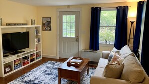 A living room with a television, bookshelf, and a window with curtains. - Private cottage nestled in center of the Vineyard (West Tisbury)