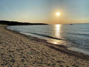 Une plage au rivage incurvé, avec une eau calme et un bateau visible au loin.