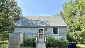 A small, single-story house with a front door, a small porch, and a window. - Private cottage nestled in center of the Vineyard (West Tisbury)