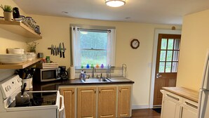 A kitchen with wooden cabinets, a stove, a microwave, and a sink. - Private cottage nestled in center of the Vineyard (West Tisbury)