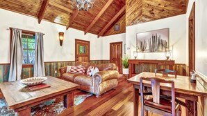 Un interior rústico con techo de madera, un sofá de cuero, una mesa de comedor y un cuadro grande.