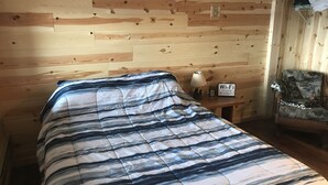 Et rum med træpaneler, en seng, en lampe, et Wi-Fi-skilt og en stol.