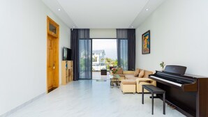 Ein modernes Wohnzimmer mit Klavier, einer Couch, einem Fernseher und einem großen Fenster mit Vorhängen.