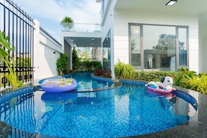 Uma piscina interior moderna com água azul cristalina, rodeada por vegetação exuberante e um edifício branco com janelas amplas.