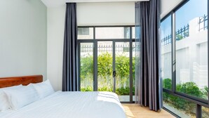 Ein Schlafzimmer mit einem großen Bett, Blick ins Grüne durch eine Schiebetür und einem modernen Interieur.