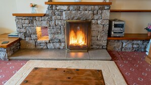 A stone fireplace with a visible fire, a wooden mantel shelf, and a small table in front. - High Butterbent Cottage -  Rural cottage that sleeps 6 guests  in 3 bedrooms (Kendal)