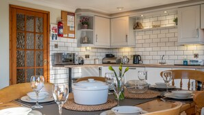 A modern kitchen with white cabinets, a microwave, toaster, and a large white pot on the counter. There is a dining table set with plates, glasses, and a vase with flowers. - High Butterbent Cottage -  Rural cottage that sleeps 6 guests  in 3 bedrooms (Kendal)
