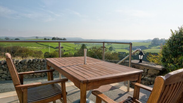 A wooden table and chairs on an outdoor terrace with a view of green fields and hills. - High Butterbent Cottage -  Rural cottage that sleeps 6 guests  in 3 bedrooms (Kendal)