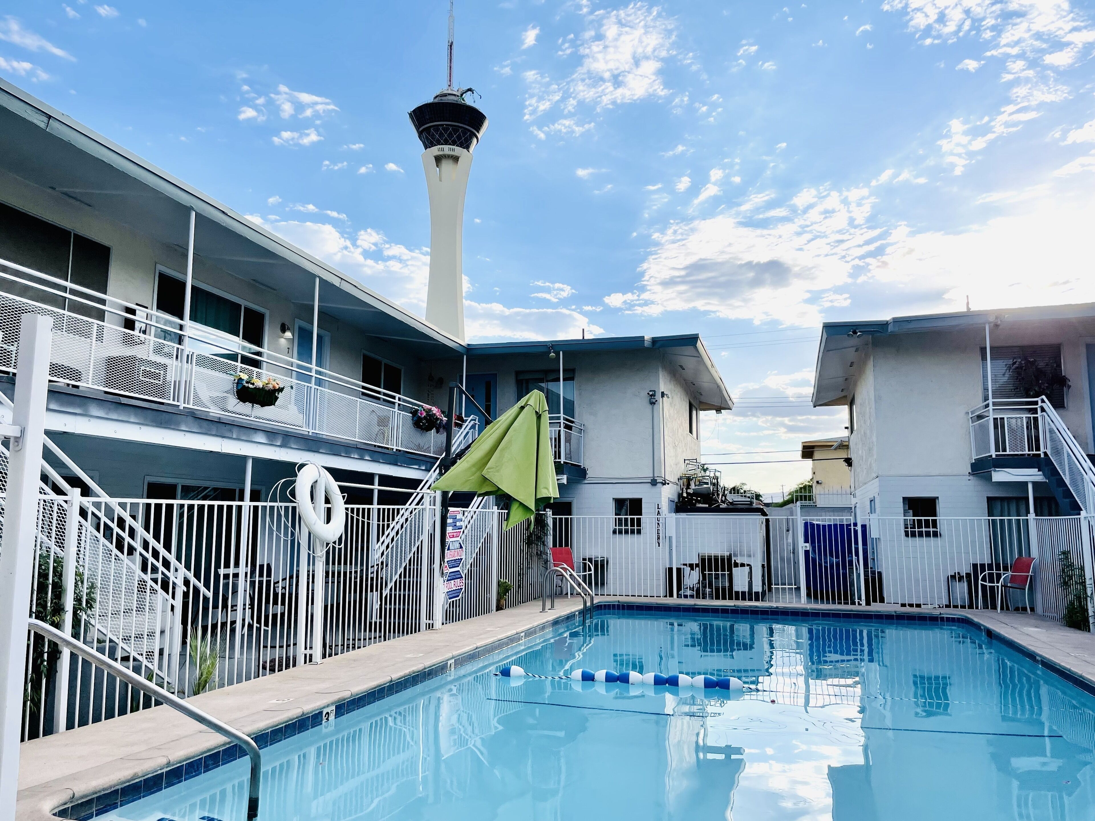 A swimming pool with a lifebuoy, a white fence, and a building with a tower.