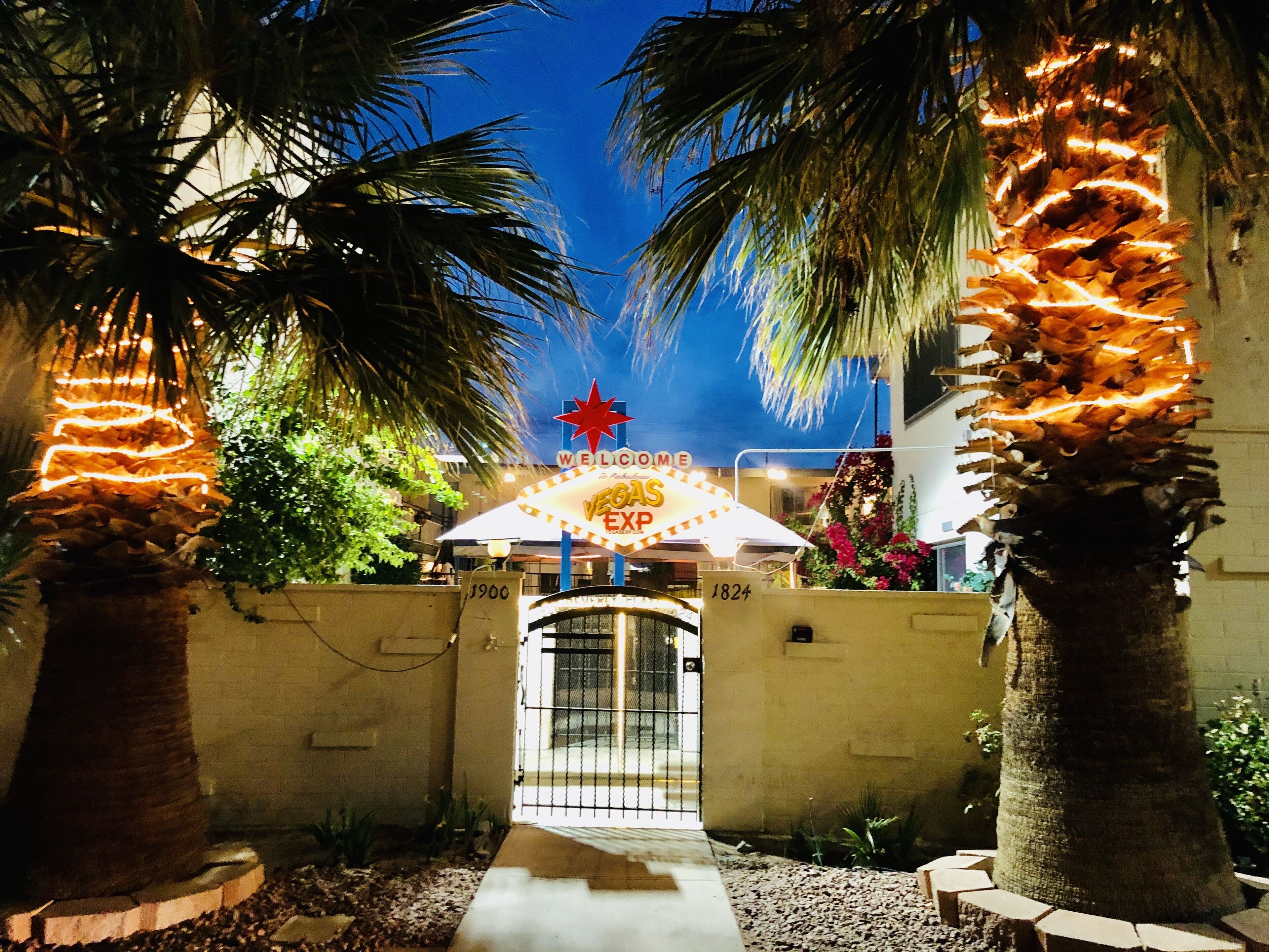 Een hotelentree met palmbomen, een bord met 'Welcome to Vegas' en een bord met 'Vegan Express'.