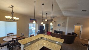 A spacious kitchen with granite countertops, a dining area with a round table and chairs, and a living room with a sofa and TV. - Cozy Island House with Heated Pool (Lake Havasu City)