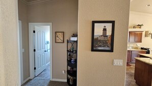 A hallway with a door leading to a room, a framed map on the wall, and a kitchen area with cabinets and a countertop. - Cozy Island House with Heated Pool (Lake Havasu City)