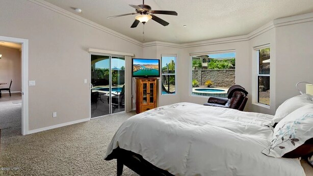 A bedroom with a large bed, a ceiling fan, a TV, and a view of a swimming pool and outdoor area. - Cozy Island House with Heated Pool (Lake Havasu City)