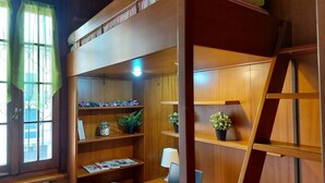 Een gezellige kamer met een stapelbed, houten planken met planten, een bureau met een laptop en een trap.