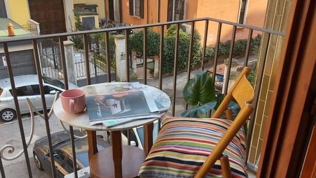 Een balkon met een tafel, een gestreept kussen en uitzicht op de straat.