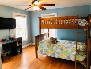 A bunk bed with a colorful quilt, a desk with a chair, a ceiling fan, and a window with blinds. - Sunny, spacious, family-friendly beach house minutes from all OOB offers (Old Orchard Beach)