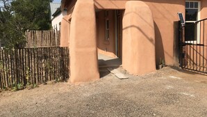 A house with a corrugated metal roof, a wooden fence, and a gravel driveway. - Casa de San Pasquale, 1800s restored terones adobe (Albuquerque)