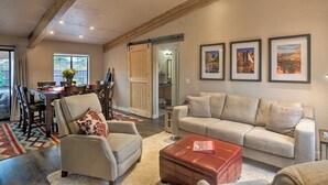 Un vaste salon comprenant un canapé, un fauteuil et un pouf, un coin repas avec une table et des chaises, et une cuisine à l’arrière-plan.