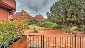 Une entrée fermée par un portail, offrant une vue sur des formations rocheuses rouges et un grand arbre au milieu d’un espace paysager aménagé.