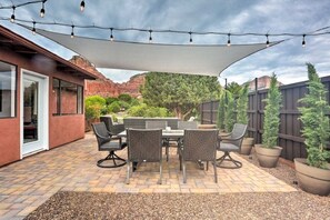 Un patio al aire libre con mesa y sillas, guirnaldas de luces y una vela parasol grande.