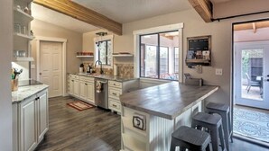 Une cuisine avec des poutres en bois, un grand îlot central, des tabourets de bar et une vue sur l’extérieur.