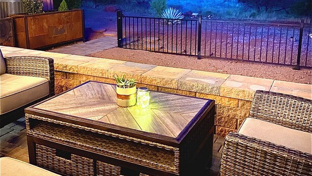 Un espace extérieur aménagé avec des meubles en osier et une table à plateau de verre, offrant une vue sur un paysage montagneux.