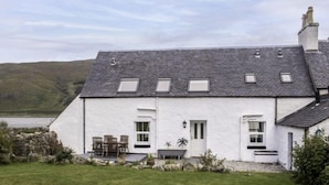 A white house with a grey roof, a small garden, and a view of hills in the background. - Old School by Interhome (Mid Skye)