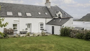 A white house with a sloped roof, a stone wall, and a grassy yard. - Old School by Interhome (Mid Skye)