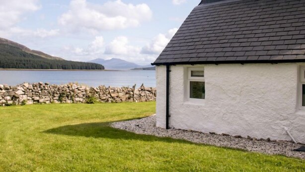 A white house with a dark roof, a stone wall, and a grassy lawn. - Old School by Interhome (Mid Skye)