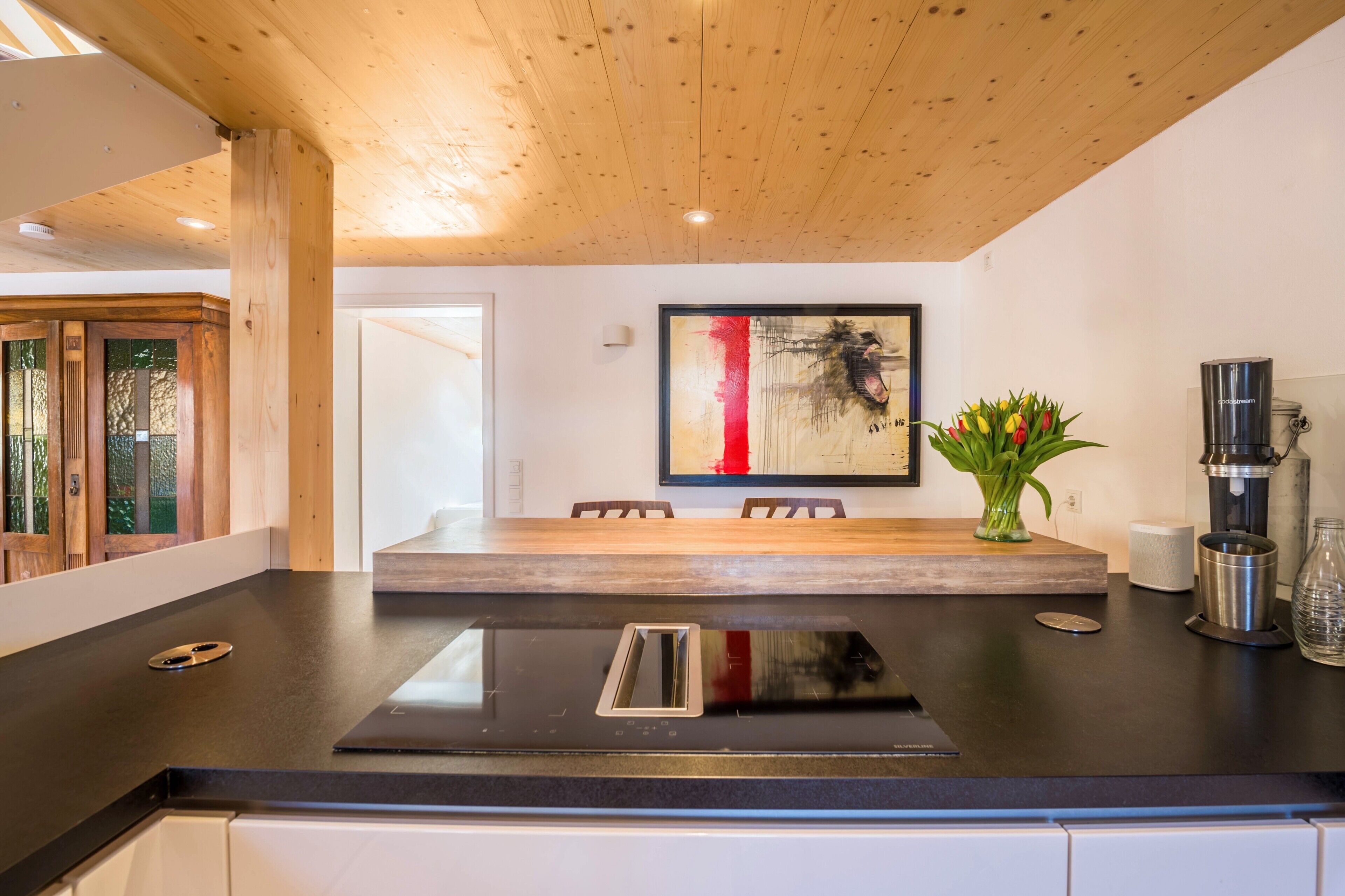 Una cocina moderna con encimera negra, techo de madera y un cuadro en la pared.