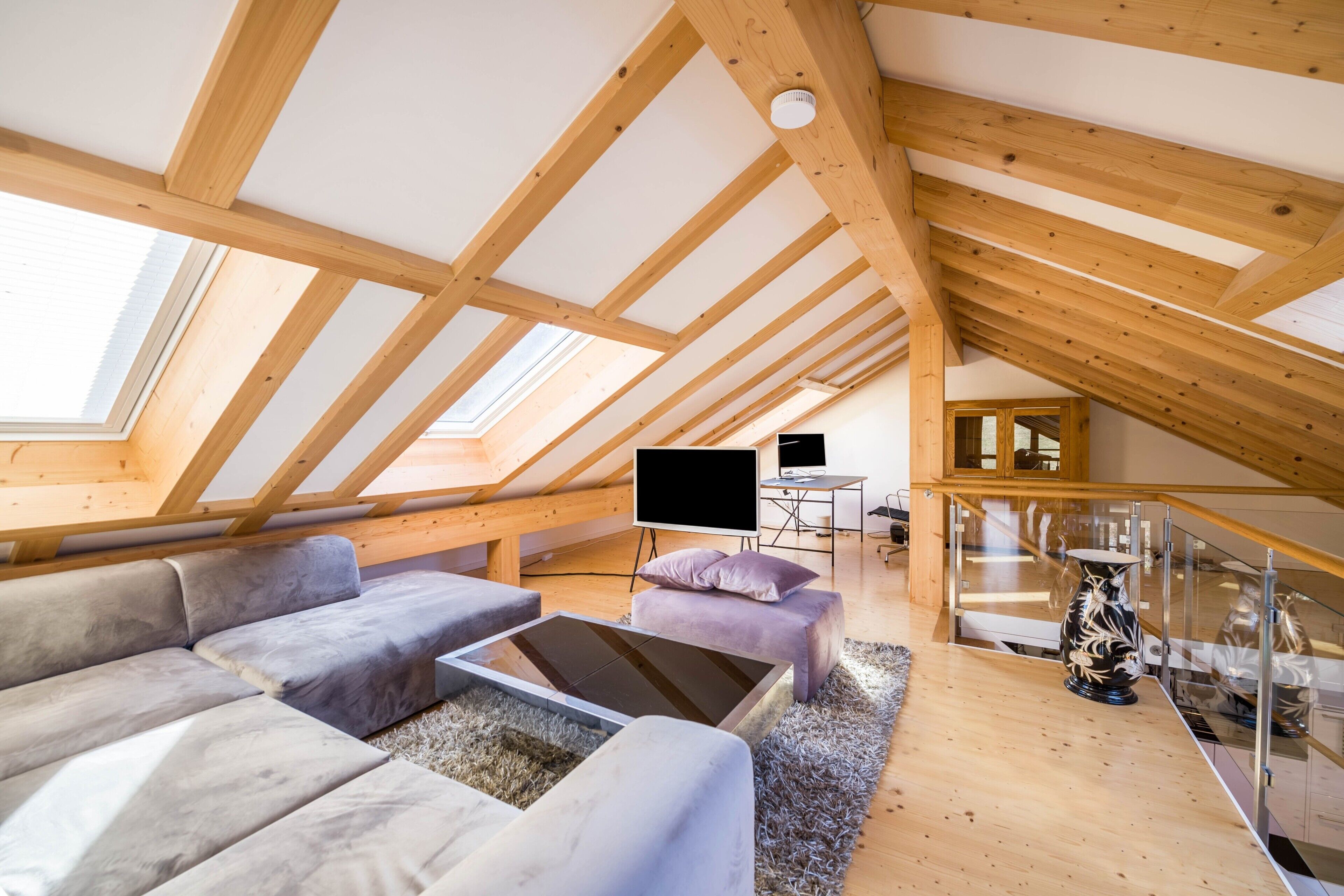A loft-style room with a wooden ceiling, a sofa, a coffee table, a TV, and a staircase.