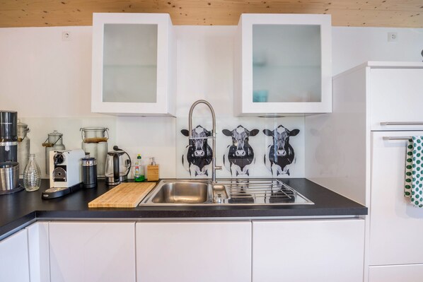 Une cuisine moderne avec un plan de travail noir, des appareils en acier inoxydable et une planche à découper en bois.